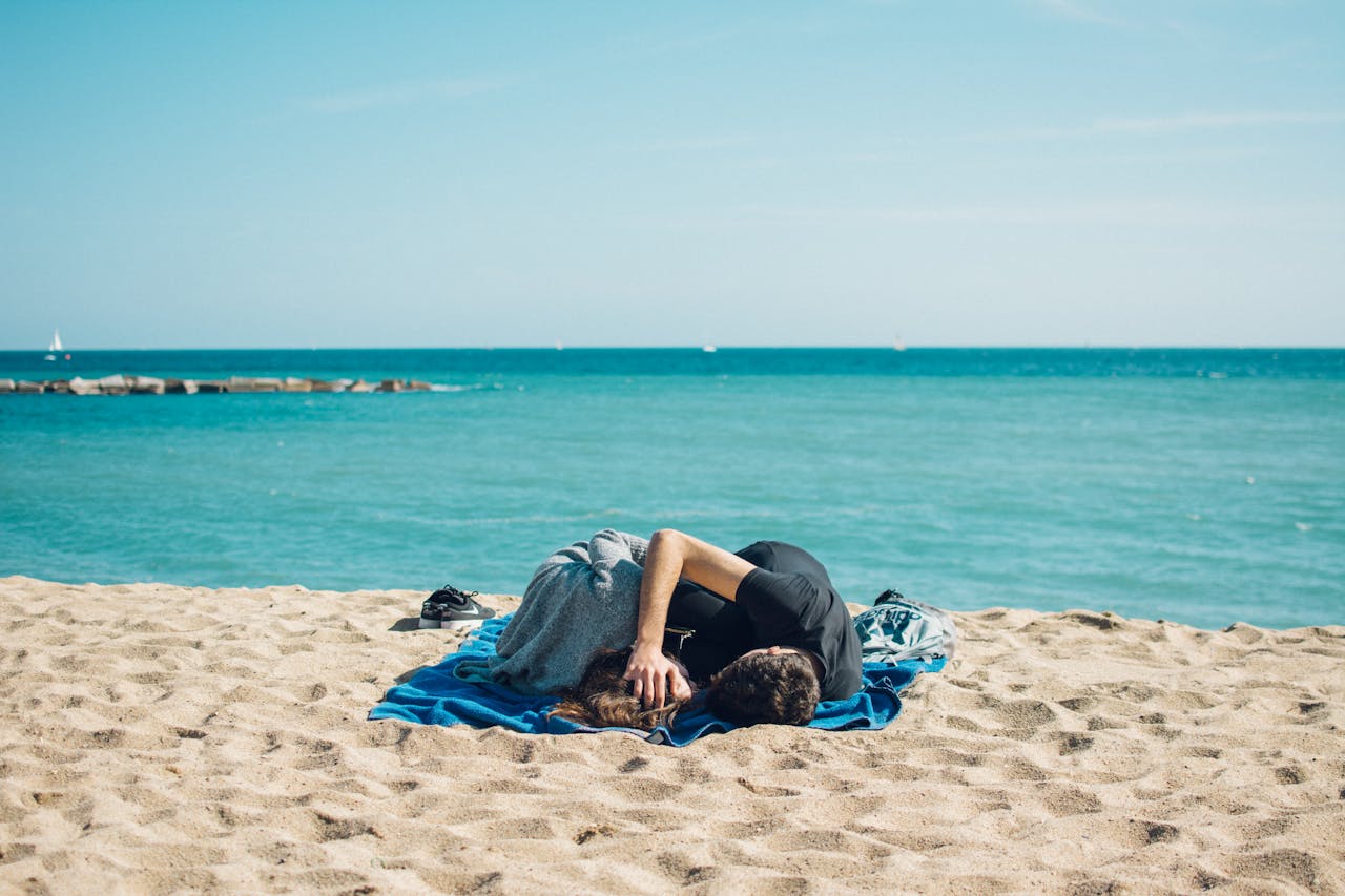 A couple enjoys a sunny day at the beach in Barcelona, Spain, resting on a blanket by the sea.